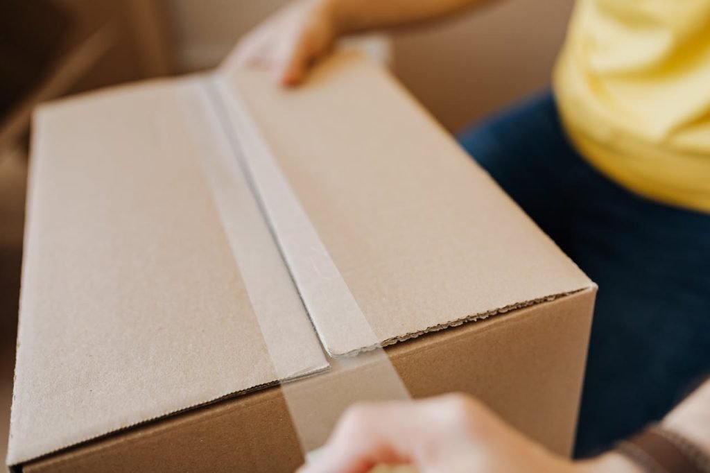 crop-man-sealing-cardboard-box-with-tape-4506249 Close-up of a person sealing a cardboard box with tape, suggesting relocation or delivery.